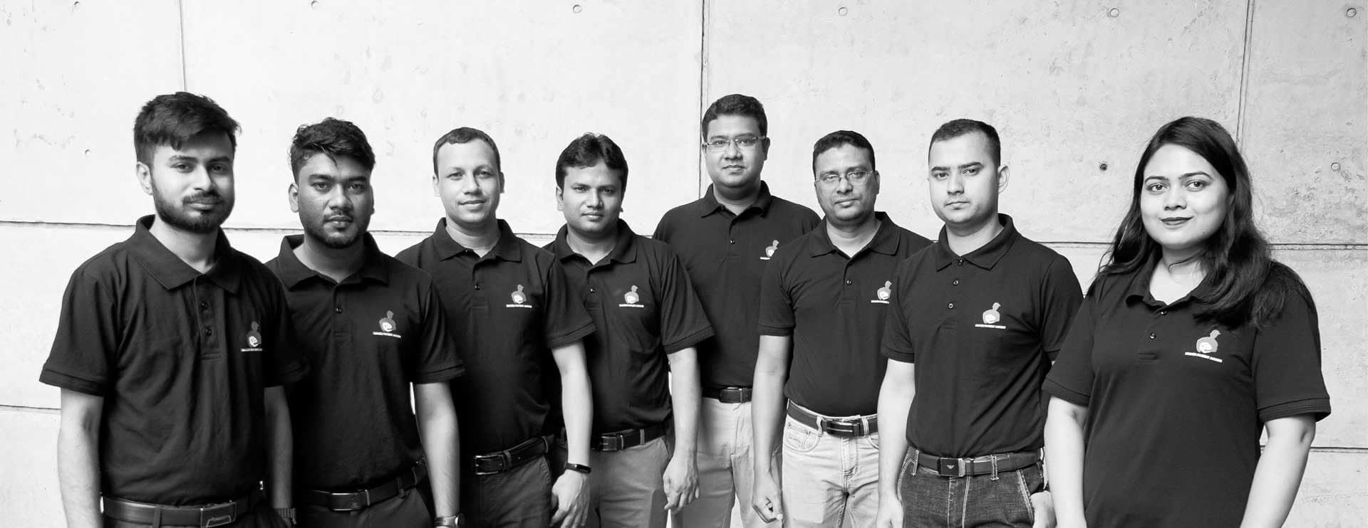 Group of eight professionals standing side by side in matching black polo shirts with the ZAS Pharma Ltd. logo, representing a dedicated team for Named Patient Services for Lifesaving Medicine Export in Bangladesh, highlighting expertise as a Pharmaceutical Exporter and Top Pharmaceutical Manufacturer in Bangladesh.